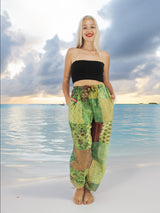 a woman standing on a beach in a black top and green pants