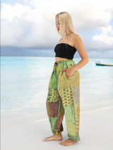 a woman standing on a beach in a black top and green pants
