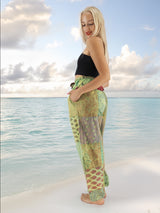 a woman standing on a beach in a black top and green pants
