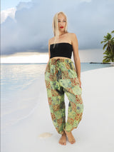 Model wearing green boho pants with geometric patterns, standing on a beach with the ocean in the background. The pants are loose and comfortable, featuring drawstrings at the waist and ankles for a relaxed fit.