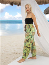 Model wearing green boho pants with geometric patterns, standing on a beach with the ocean in the background. The pants are loose and comfortable, featuring drawstrings at the waist and ankles for a relaxed fit.