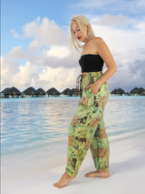 Model wearing green boho pants with geometric patterns, standing on a beach with the ocean in the background. The pants are loose and comfortable, featuring drawstrings at the waist and ankles for a relaxed fit.