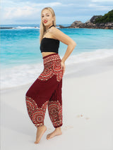 a woman standing on a beach wearing a black top and red pants