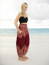 a woman standing on a beach wearing a black top and red pants
