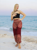 a woman standing on the beach in a black top and red pants