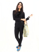 Elegant aqua and gold canvas handbag with leather handles, made in Italy, resting against a woman in a black outfit.