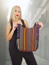 Back view of a handmade cross body cotton hemp hippie handbag purse with intricate woven patterns, held by a model in a sunlit European alley.