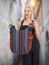 Back view of a handmade cross body cotton hemp hippie handbag featuring a striped boho pattern, held by a cheerful model in a charming alleyway.