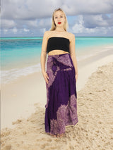 a woman standing on a beach wearing a purple skirt