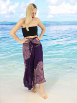 a woman standing on a beach wearing a purple skirt
