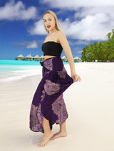 a woman standing on a beach wearing a purple skirt