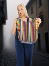 Back view of a handmade cotton hemp hippie handbag featuring a striped tribal pattern, displayed by a model in a vintage alleyway.