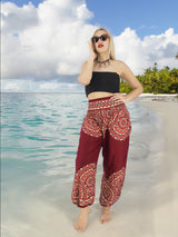 a woman standing on a beach wearing a black top and red pants