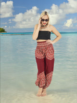 a woman standing on a beach wearing a black top and red pants