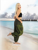 Model wearing green boho pants with geometric patterns, standing on a beach with the ocean in the background. The pants are loose and comfortable, featuring drawstrings at the waist and elastic at the ankles for a relaxed fit