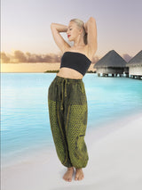 Model wearing green boho pants with geometric patterns, standing on a beach with the ocean in the background. The pants are loose and comfortable, featuring drawstrings at the waist and elastic at the ankles for a relaxed fit