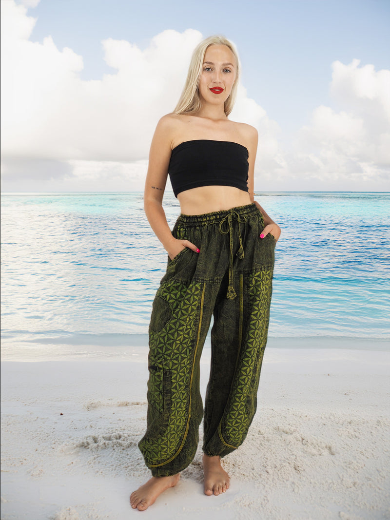 Model wearing green boho pants with geometric patterns, standing on a beach with the ocean in the background. The pants are loose and comfortable, featuring drawstrings at the waist and elastic at the ankles for a relaxed fit