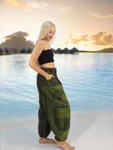 Model wearing green boho pants with geometric patterns, standing on a beach with the ocean in the background. The pants are loose and comfortable, featuring drawstrings at the waist and elastic at the ankles for a relaxed fit