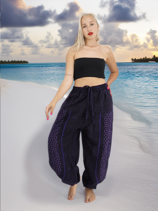 a woman standing on a beach wearing a black top and purple pants