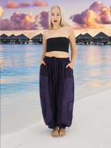 a woman standing on a beach wearing a black top and purple pants