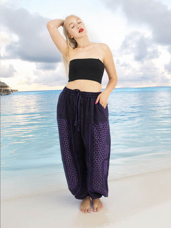 a woman standing on a beach wearing a black top and purple pants