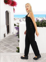 a woman in a black jumpsuit standing by a white wall