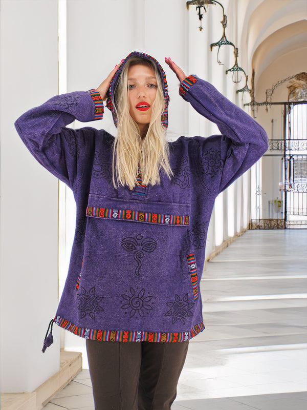 Woman in a purple bohemian-style hoodie with colorful embroidery and patterns, smiling and holding the hood in a bright outdoor setting