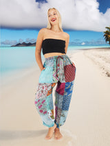 Woman wearing vibrant bohemian cotton patchwork pants standing on the beach with the ocean in the background.