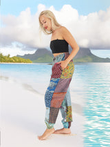 Woman wearing vibrant bohemian cotton patchwork pants standing on the beach with the ocean in the background.