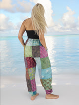 Woman wearing vibrant bohemian cotton patchwork pants standing on the beach with the ocean in the background.