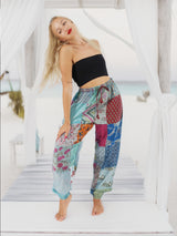 Woman wearing vibrant bohemian cotton patchwork pants standing on the beach with the ocean in the background.