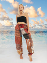 Woman wearing vibrant bohemian cotton patchwork pants standing on the beach with the ocean in the background.