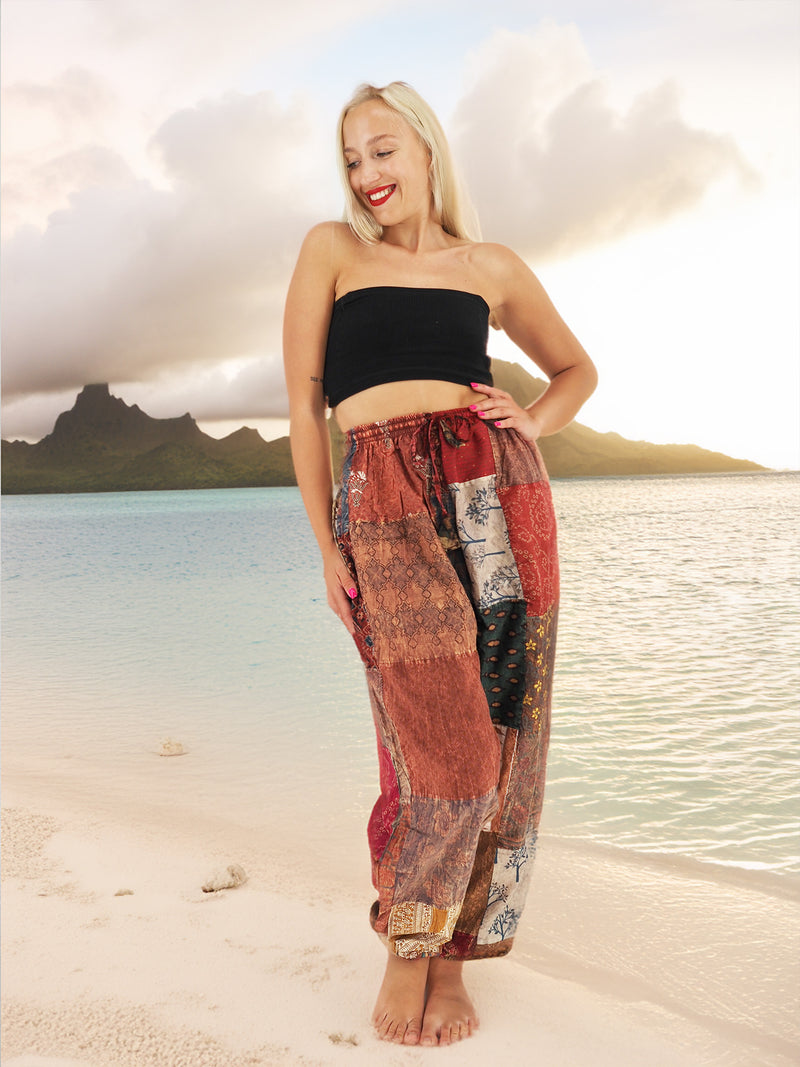 Woman wearing vibrant bohemian cotton patchwork pants standing on the beach with the ocean in the background.