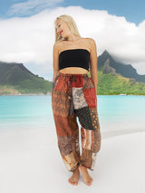 Woman wearing vibrant bohemian cotton patchwork pants standing on the beach with the ocean in the background.