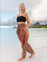 a woman standing on a beach in a black top and patterned pants