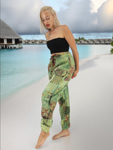 a woman standing on a beach in a black top and green pants