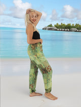 a woman standing on a beach in a black top and green pants