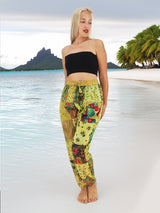 Model wearing green boho pants with geometric patterns, standing on a beach with the ocean in the background. The pants are loose and comfortable, featuring drawstrings at the waist and ankles for a relaxed fit.