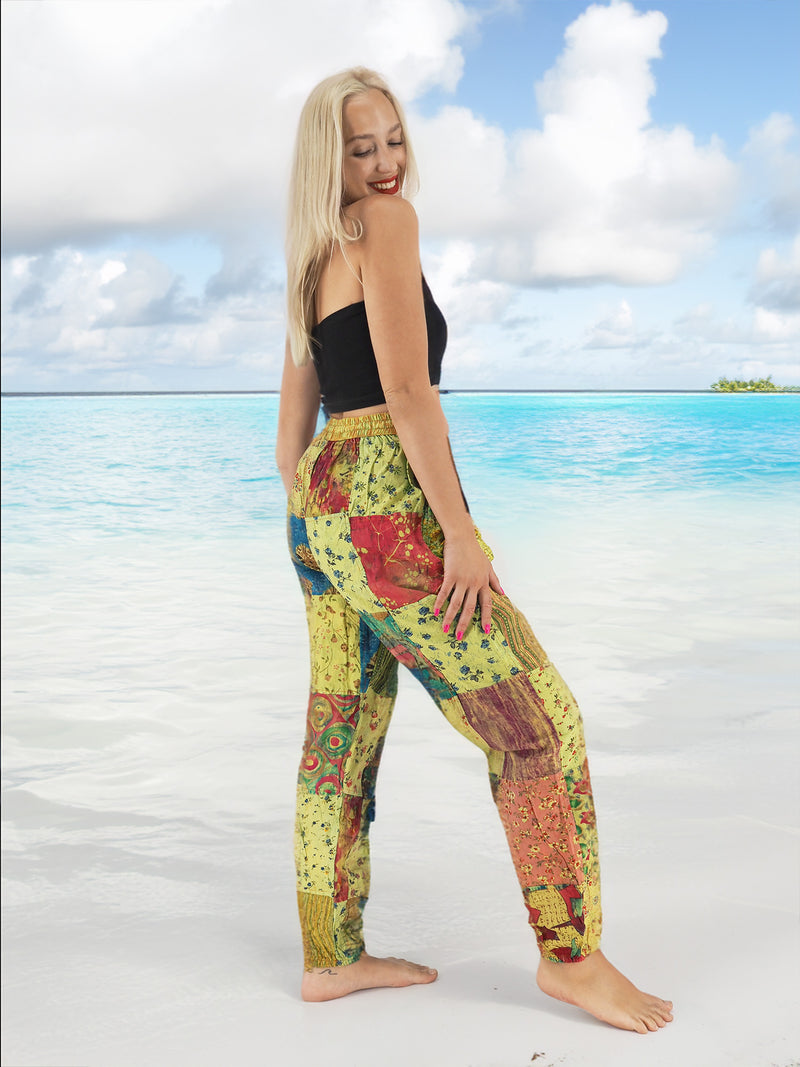 Model wearing green boho pants with geometric patterns, standing on a beach with the ocean in the background. The pants are loose and comfortable, featuring drawstrings at the waist and ankles for a relaxed fit.