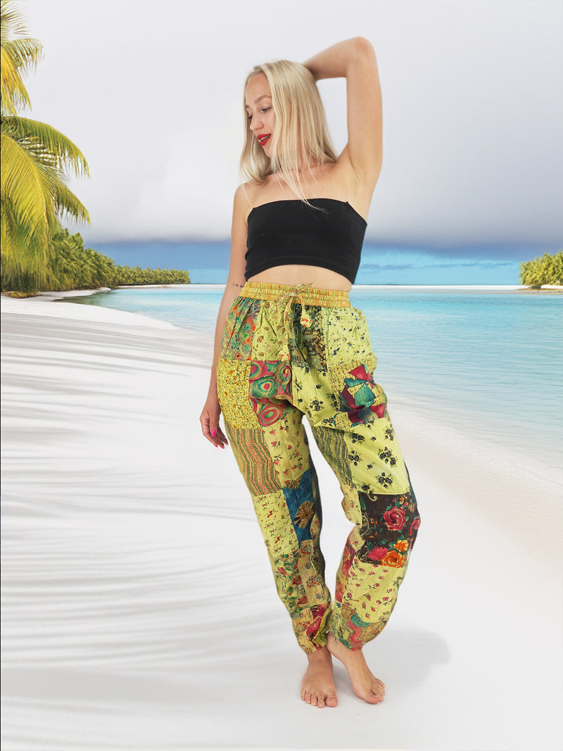 Model wearing green boho pants with geometric patterns, standing on a beach with the ocean in the background. The pants are loose and comfortable, featuring drawstrings at the waist and ankles for a relaxed fit.