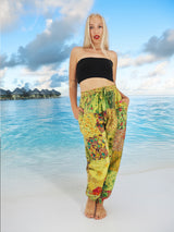 Model wearing green boho pants with geometric patterns, standing on a beach with the ocean in the background. The pants are loose and comfortable, featuring drawstrings at the waist and ankles for a relaxed fit.