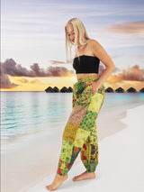 Model wearing green boho pants with geometric patterns, standing on a beach with the ocean in the background. The pants are loose and comfortable, featuring drawstrings at the waist and ankles for a relaxed fit.