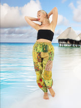 Model wearing green boho pants with geometric patterns, standing on a beach with the ocean in the background. The pants are loose and comfortable, featuring drawstrings at the waist and ankles for a relaxed fit.