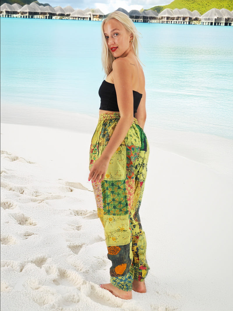 Model wearing green boho pants with geometric patterns, standing on a beach with the ocean in the background. The pants are loose and comfortable, featuring drawstrings at the waist and ankles for a relaxed fit.